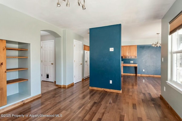 unfurnished living room featuring dark wood-type flooring, arched walkways, a chandelier, and baseboards