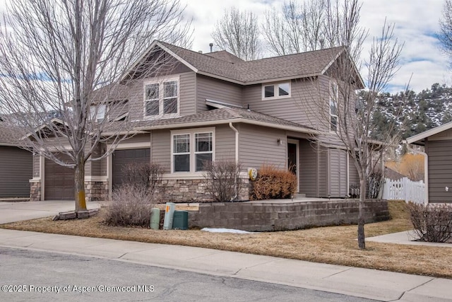 view of front of house with a shingled roof, concrete driveway, an attached garage, fence, and stone siding