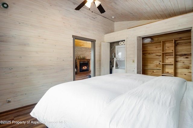 bedroom with wooden ceiling, wood finished floors, a lit fireplace, vaulted ceiling, and wood walls