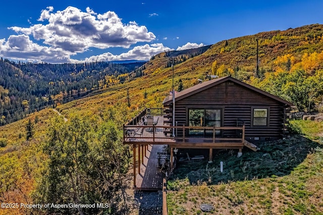 rear view of house with a deck with mountain view, stairs, crawl space, log exterior, and a wooded view