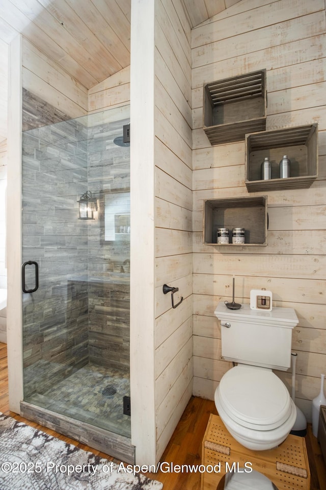 bathroom with wooden walls, a shower stall, toilet, and wood finished floors