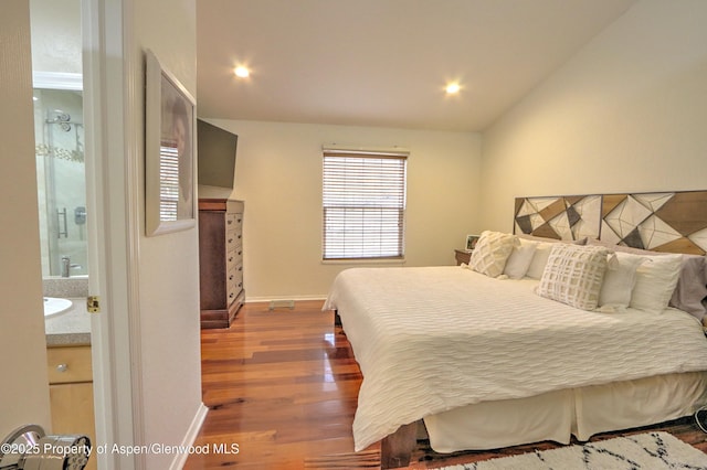 bedroom featuring baseboards, vaulted ceiling, wood finished floors, and ensuite bathroom