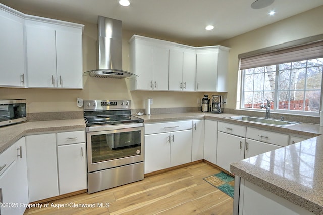 kitchen featuring recessed lighting, stainless steel appliances, a sink, light wood-style floors, and wall chimney range hood
