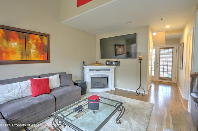 living room with recessed lighting, light wood-style flooring, baseboards, and a glass covered fireplace