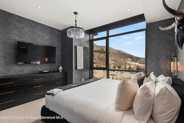 bedroom featuring light carpet, a mountain view, a wall of windows, and a chandelier