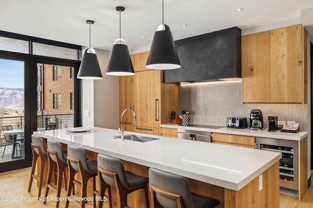 kitchen featuring wine cooler, hanging light fixtures, sink, and an island with sink