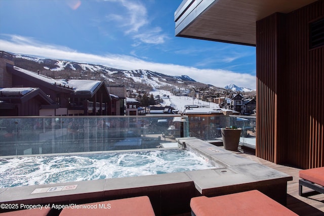 snow covered patio with an outdoor hot tub, a mountain view, and a balcony