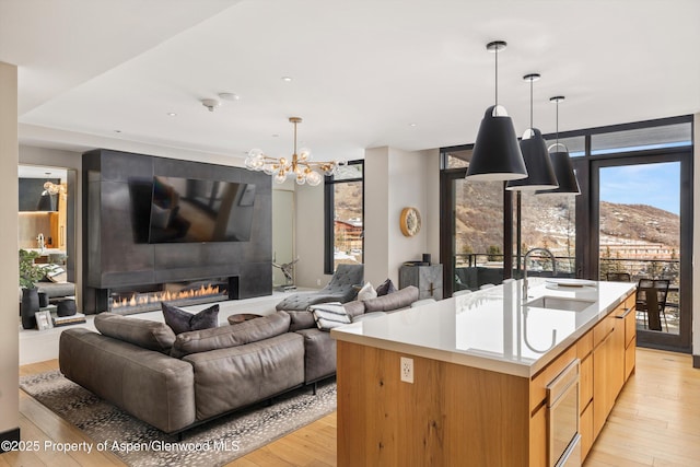 kitchen featuring pendant lighting, sink, light hardwood / wood-style flooring, a kitchen island with sink, and a fireplace