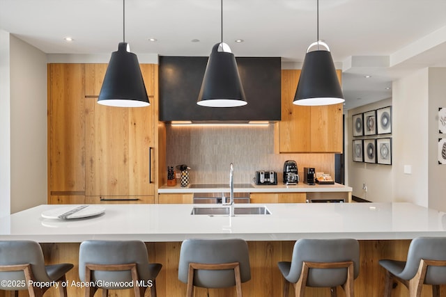 kitchen with a center island with sink, sink, hanging light fixtures, and backsplash