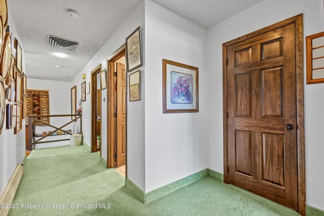 hallway featuring a textured ceiling, light colored carpet, and a baseboard radiator