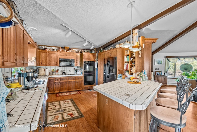 kitchen featuring backsplash, black appliances, tile countertops, light hardwood / wood-style flooring, and vaulted ceiling with beams