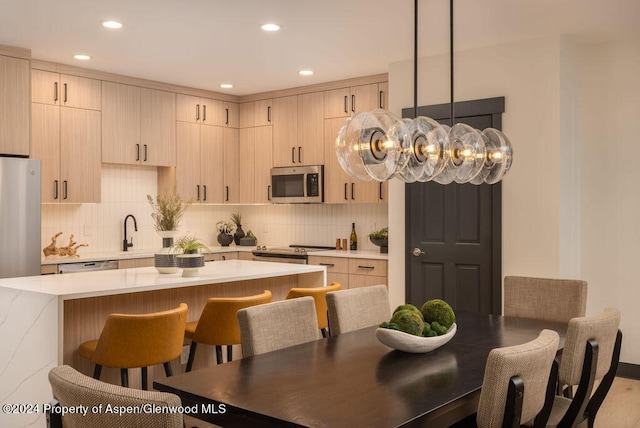 kitchen featuring hanging light fixtures, a kitchen island, stainless steel appliances, and light brown cabinets