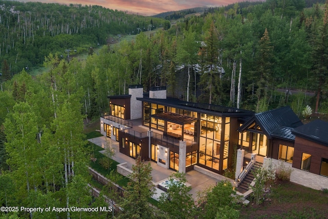 1234 Wood Rd, Snowmass Village, CO 81615 - back of house at dusk with a view of trees, a patio, a chimney, stairway, and metal roof