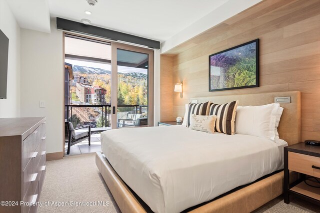 bedroom featuring access to exterior, wooden walls, a mountain view, and light colored carpet