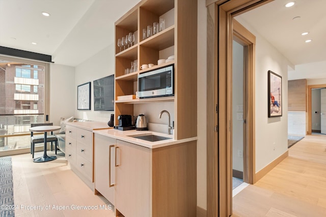 kitchen featuring stainless steel microwave, light hardwood / wood-style flooring, light brown cabinets, and sink