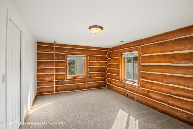 carpeted empty room featuring rustic walls and a wealth of natural light