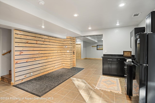 kitchen with light tile patterned floors, black fridge, and wooden walls