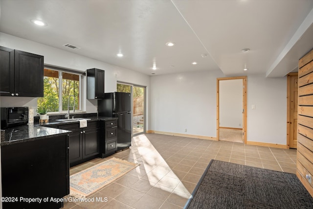 kitchen featuring light tile patterned floors, dark stone counters, black appliances, and sink