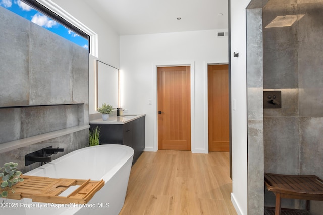 bathroom featuring vanity, walk in shower, a freestanding bath, and wood finished floors