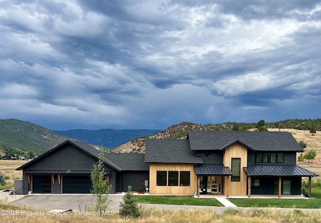 view of front facade featuring a shingled roof, a standing seam roof, a mountain view, and an attached garage