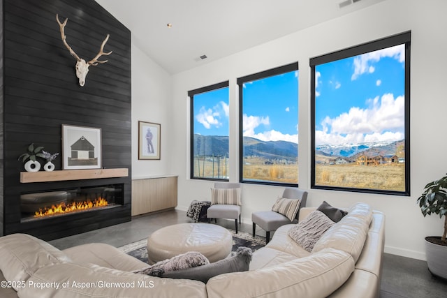 living room with a fireplace, lofted ceiling, finished concrete floors, a mountain view, and baseboards