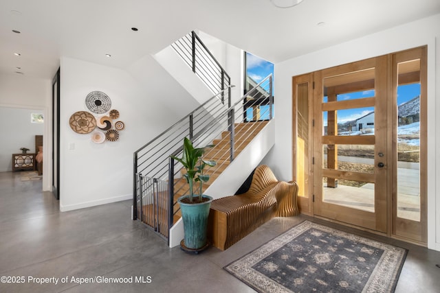 foyer with baseboards, concrete floors, and stairway