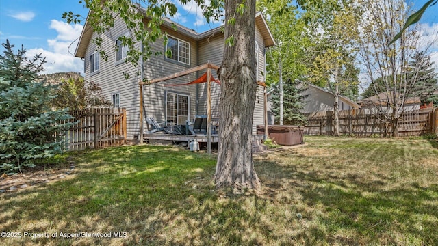 rear view of house featuring a hot tub, a fenced backyard, a lawn, and a deck