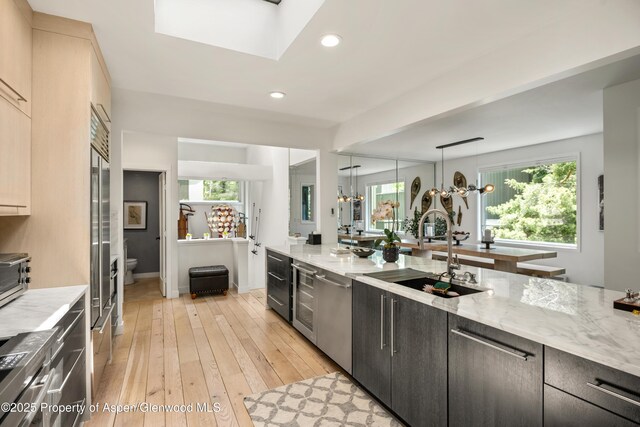 kitchen featuring sink, hanging light fixtures, a skylight, light wood-type flooring, and light stone counters