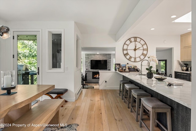 kitchen featuring a breakfast bar, light brown cabinets, light wood-type flooring, a fireplace, and kitchen peninsula