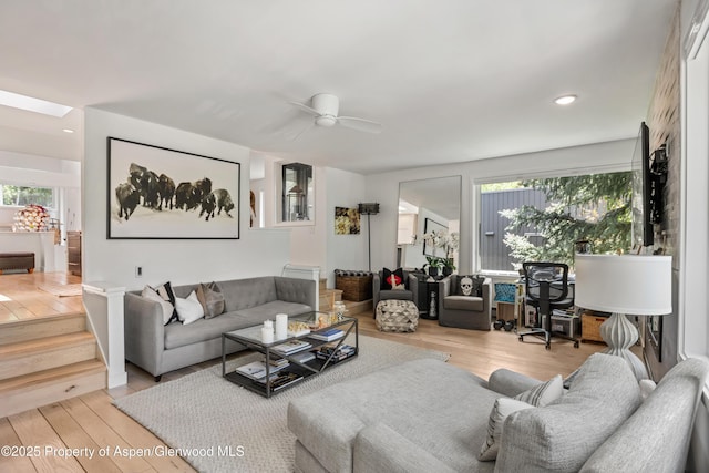 living room with light hardwood / wood-style flooring, ceiling fan, a skylight, and a healthy amount of sunlight