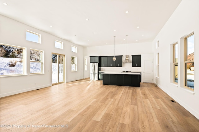 kitchen with pendant lighting, stainless steel refrigerator, a high ceiling, a center island with sink, and light wood-type flooring