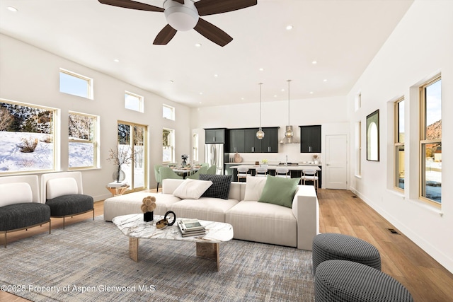 living room featuring a towering ceiling, light hardwood / wood-style flooring, and ceiling fan