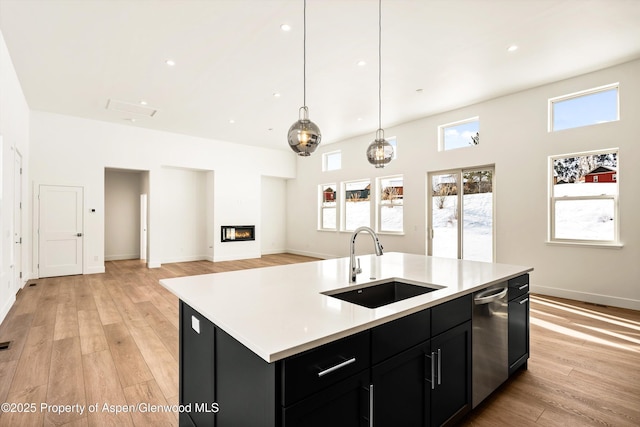 kitchen with sink, light hardwood / wood-style flooring, dishwasher, an island with sink, and pendant lighting