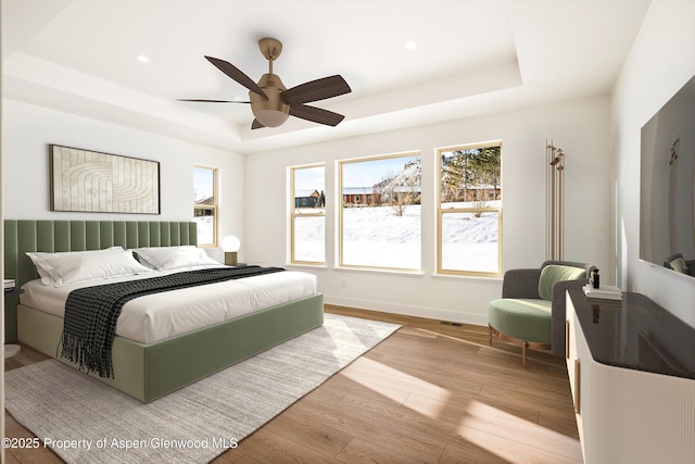 bedroom with light hardwood / wood-style flooring, ceiling fan, and a tray ceiling