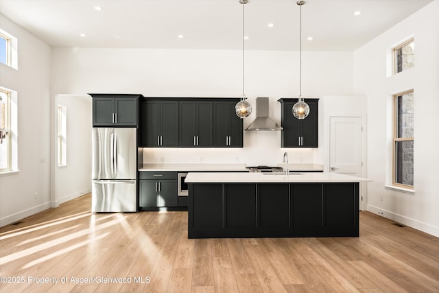 kitchen with light countertops, a sink, freestanding refrigerator, a high ceiling, and wall chimney exhaust hood