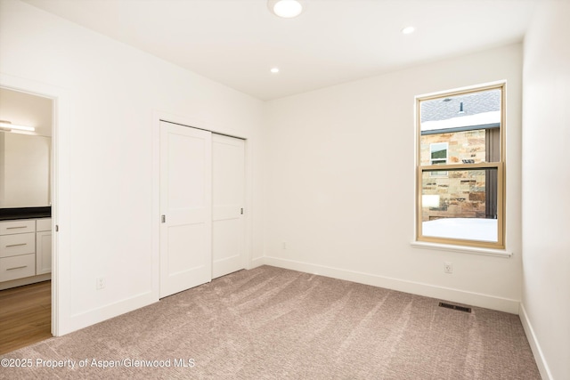 unfurnished bedroom featuring light carpet, ensuite bath, and a closet