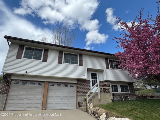 bi-level home with an attached garage, concrete driveway, brick siding, and a front yard