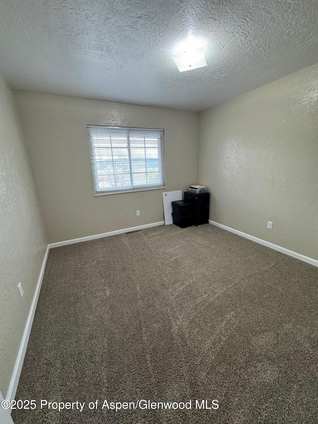carpeted empty room with a textured ceiling, baseboards, and a textured wall