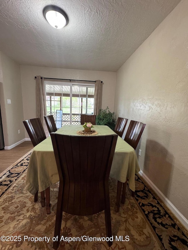 dining space featuring a textured ceiling, baseboards, and wood finished floors