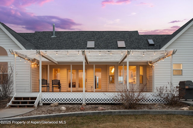 back of house at dusk with a porch, a pergola, and roof with shingles