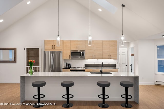 kitchen featuring light brown cabinets, light wood-style flooring, a sink, appliances with stainless steel finishes, and a kitchen bar