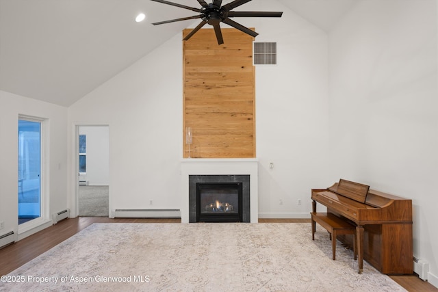 living room with a baseboard heating unit, a glass covered fireplace, wood finished floors, and visible vents