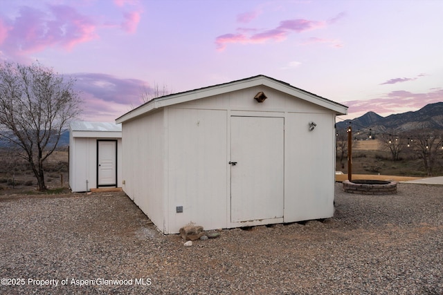 outdoor structure at dusk featuring a storage shed, an outbuilding, a mountain view, and an outdoor fire pit