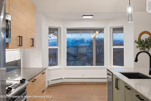 kitchen featuring a sink, a baseboard heating unit, wood finished floors, appliances with stainless steel finishes, and light stone countertops