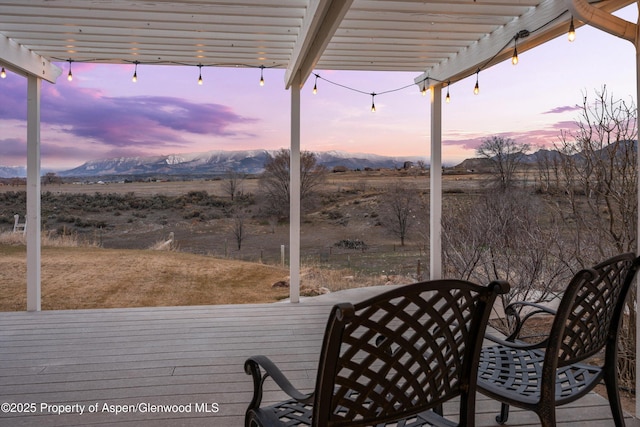 deck at dusk featuring a mountain view, a rural view, and a pergola