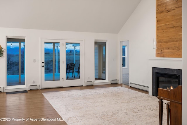 unfurnished living room featuring a baseboard heating unit, wood finished floors, baseboard heating, and a glass covered fireplace