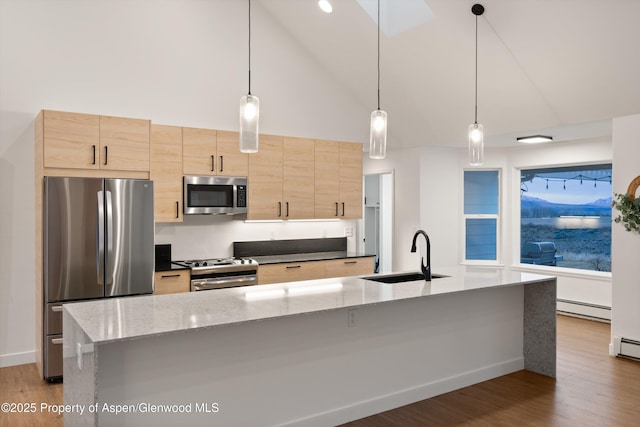 kitchen featuring light wood finished floors, light brown cabinetry, baseboard heating, appliances with stainless steel finishes, and a sink