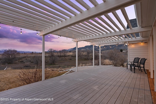 deck at dusk featuring a mountain view and a pergola