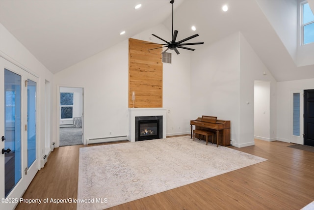 unfurnished living room featuring wood finished floors, visible vents, high vaulted ceiling, a glass covered fireplace, and a baseboard heating unit