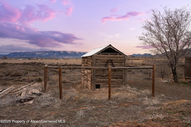 outdoor structure at dusk featuring a rural view, a mountain view, an outdoor structure, and fence